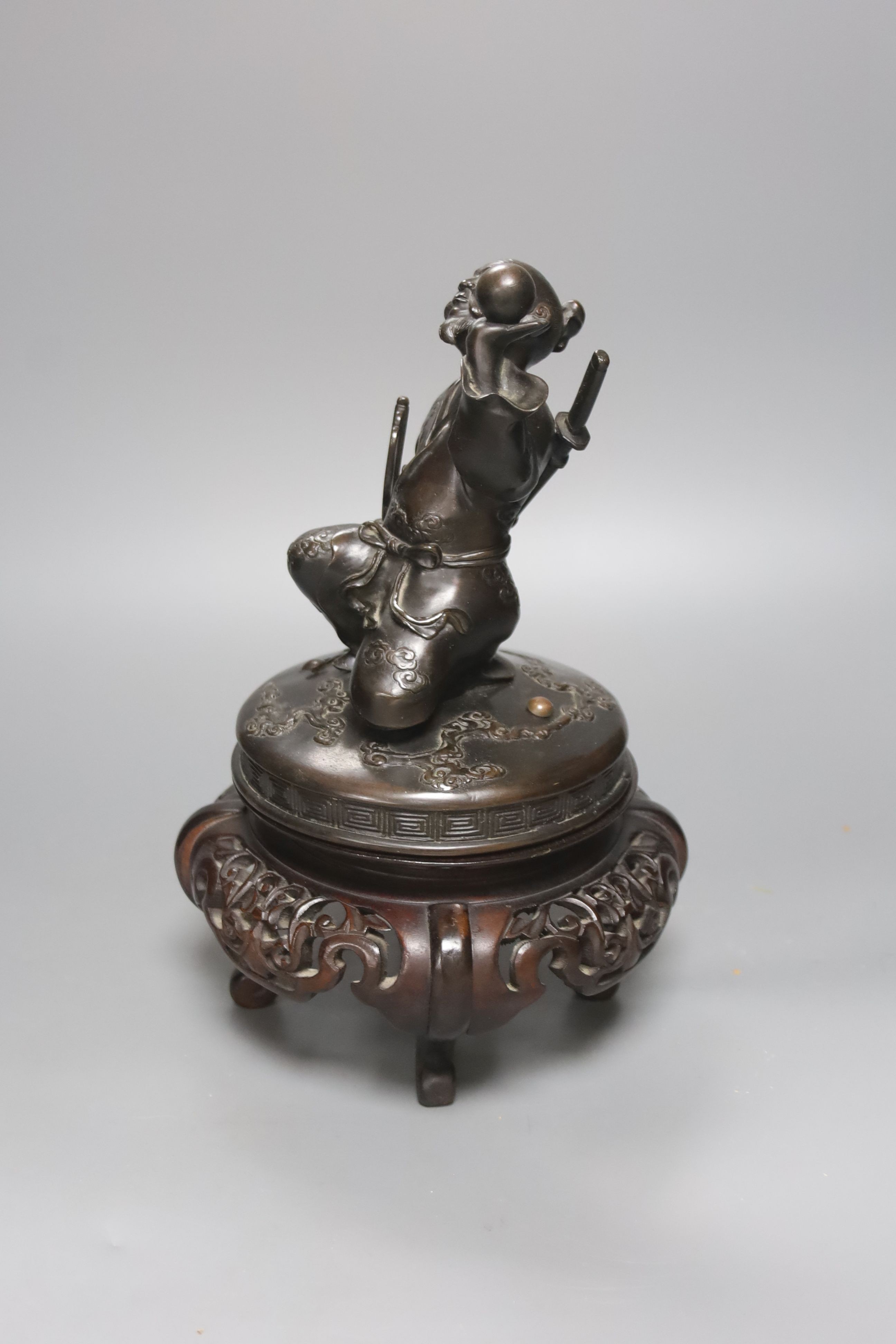 A Japanese bronze cover modelled as a samurai general, Meiji period, holding a fan and a ball, wood stand 28cm total height